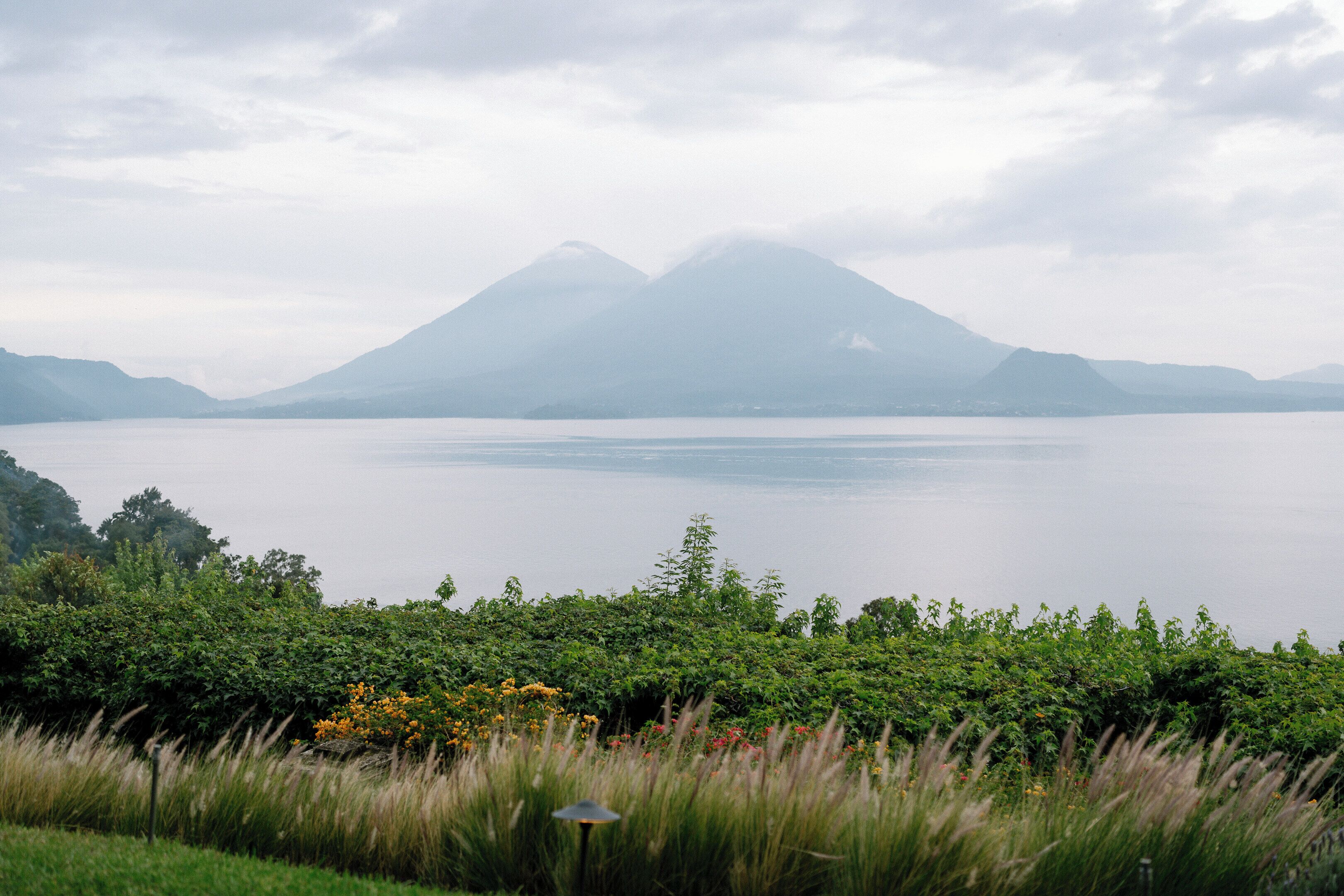 Un lago con montañas al fondo y vegetación densa en primer plano.
