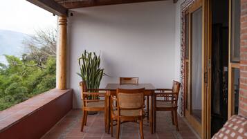 A wooden dining table with four chairs and a potted plant on a balcony with a tiled floor.
