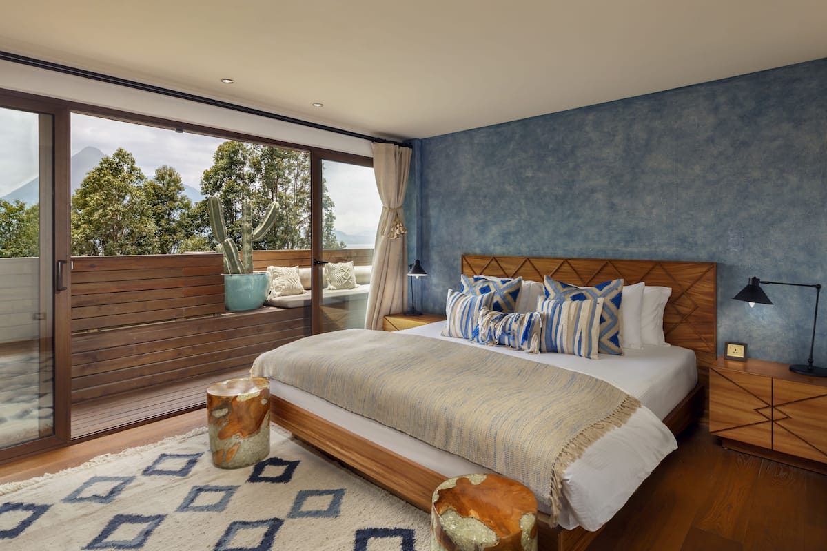 Une chambre à coucher avec un grand lit, une tête de lit en bois et une vue sur les arbres et les montagnes par la fenêtre.
