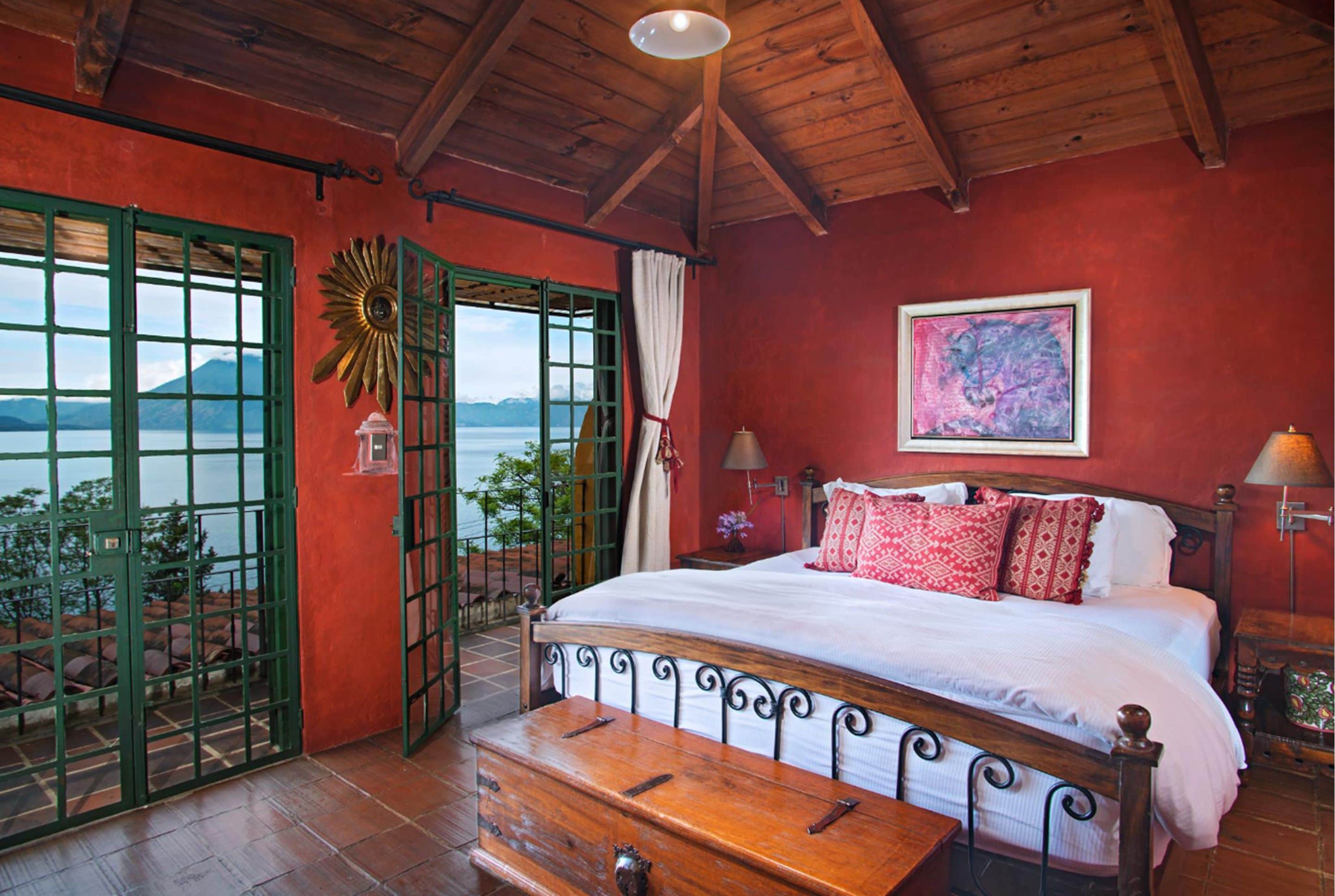 A bedroom with a wooden bed, a view of the sea, and a green gate.