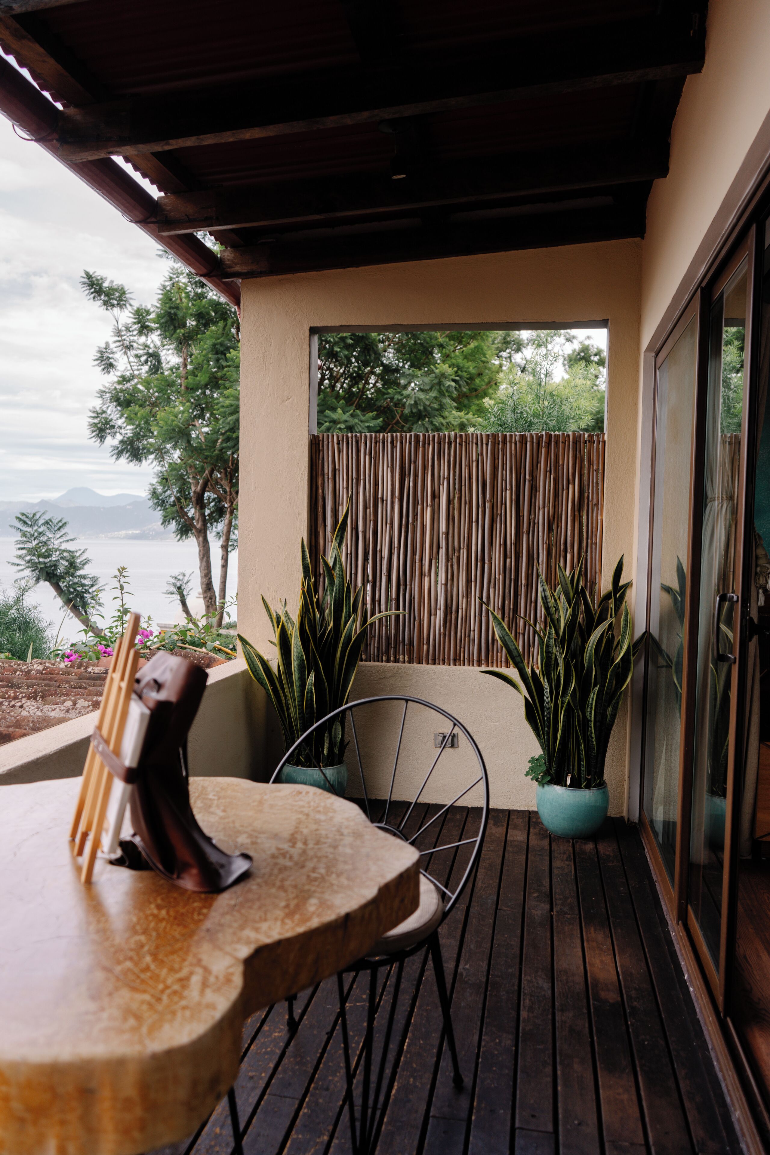 Una terraza de madera con una mesa y sillas, plantas en macetas y vistas al mar y a las montañas.
