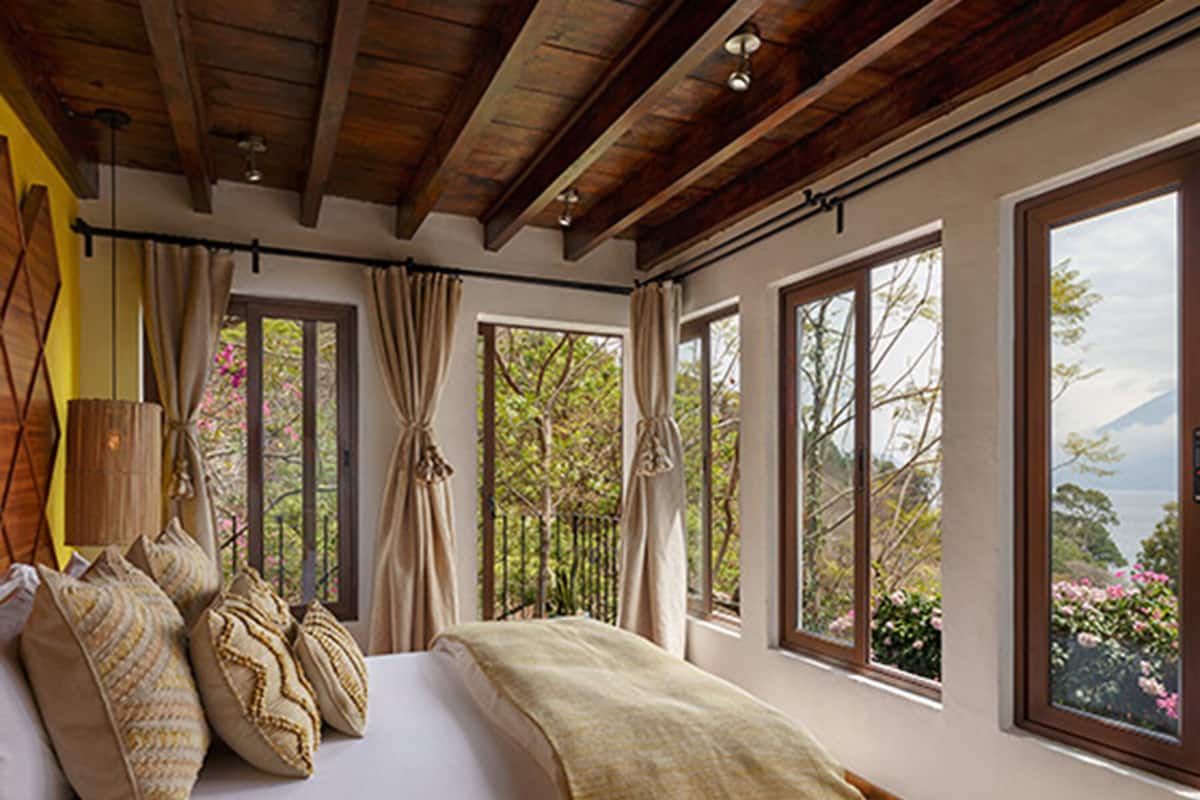Une chambre avec un grand lit, de nombreuses fenêtres et une vue sur les arbres et les montagnes.