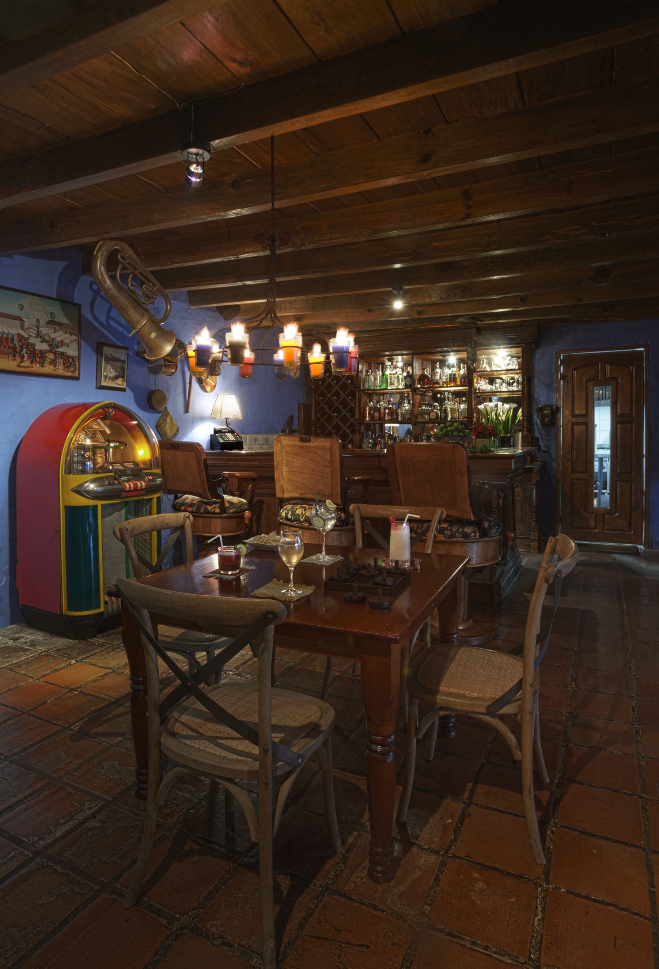 A rustic bar area with wooden furniture, a jukebox, and a variety of bottles on shelves.