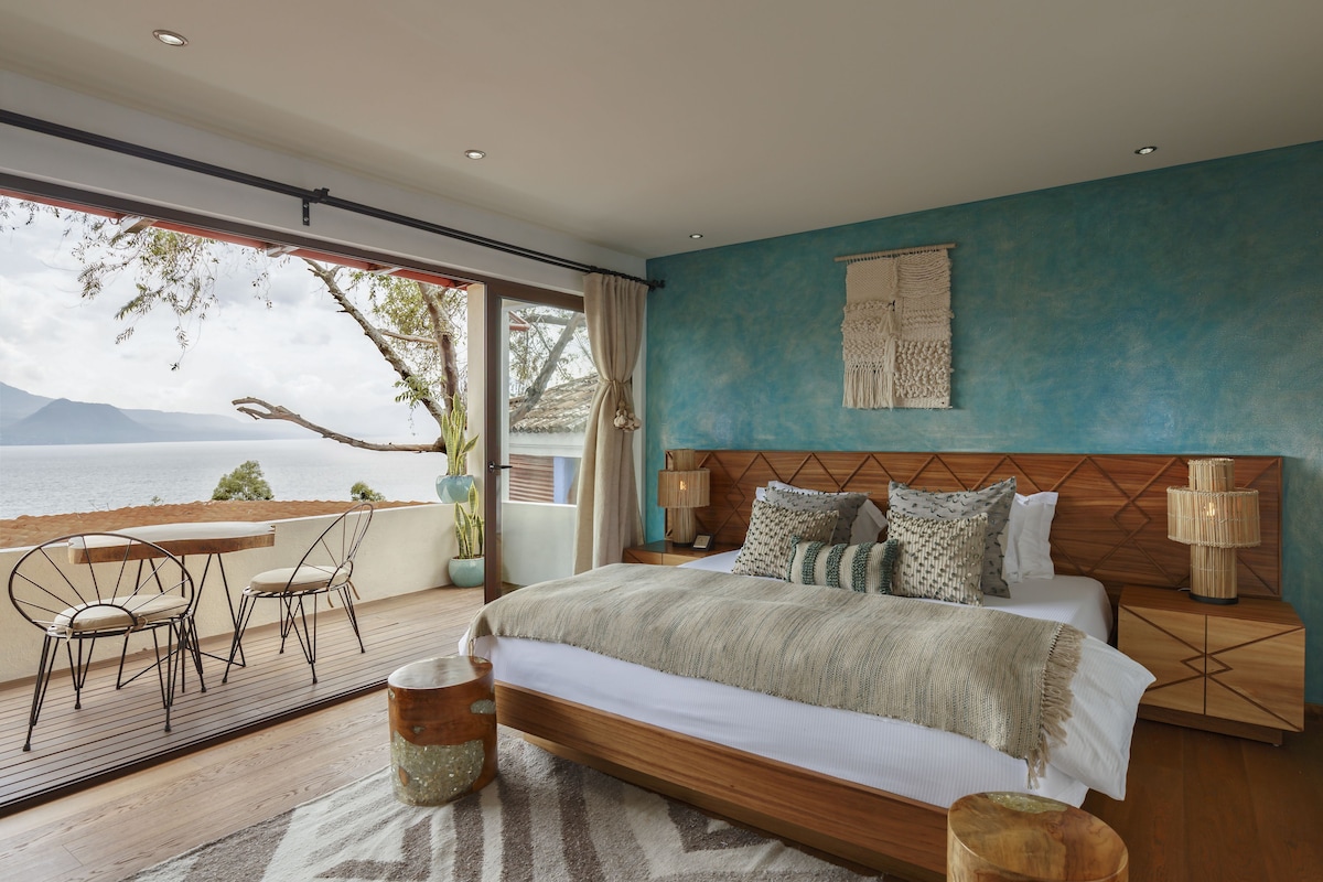 Een slaapkamer met een groot bed, houten hoofdbord en uitzicht op zee.