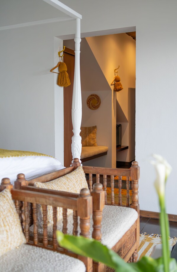 A bedroom with a four-poster bed, a wooden chair, and a mirror reflecting a cozy sitting area.