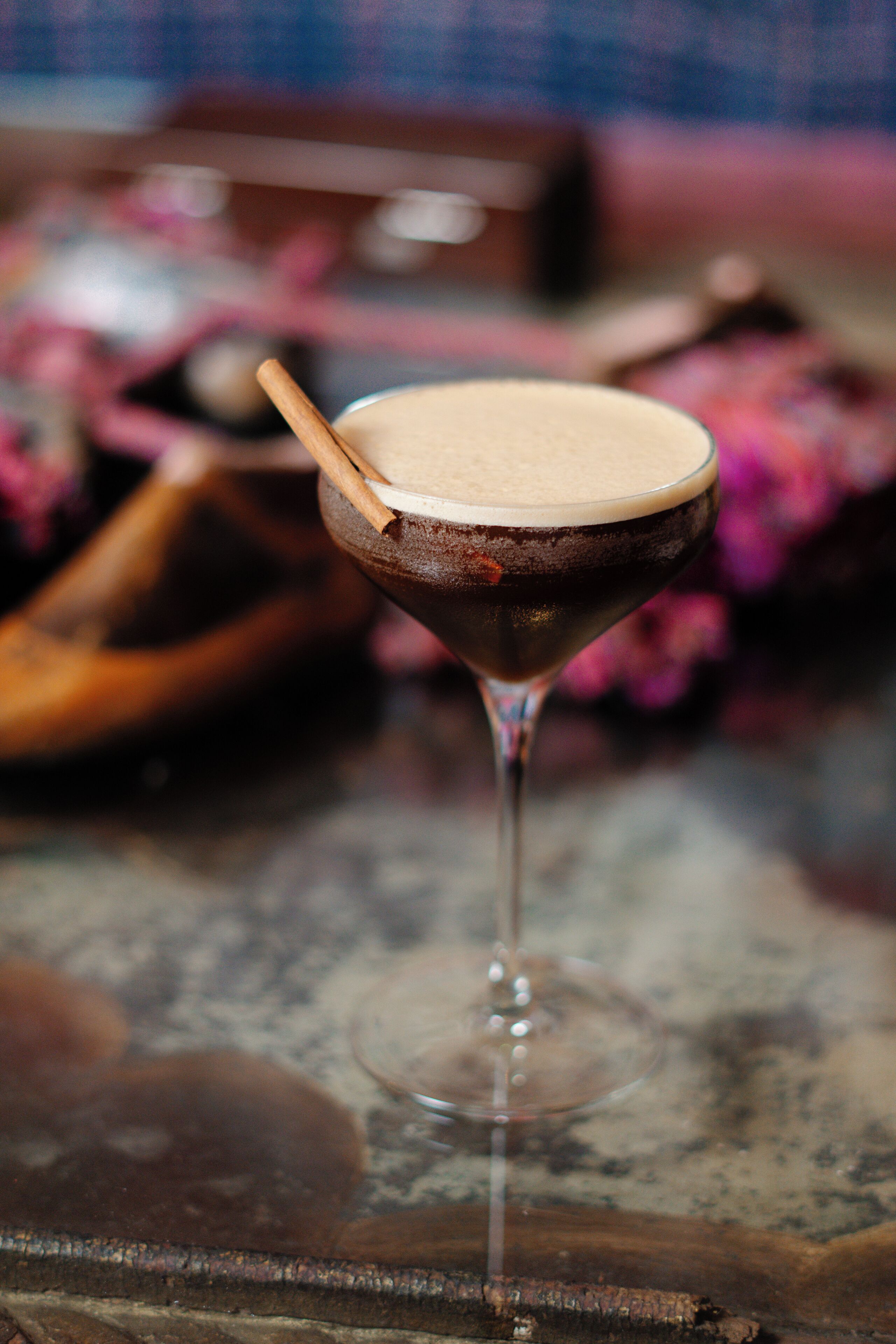 A martini glass with a wooden stick on the rim, placed on a textured surface with a blurred background.