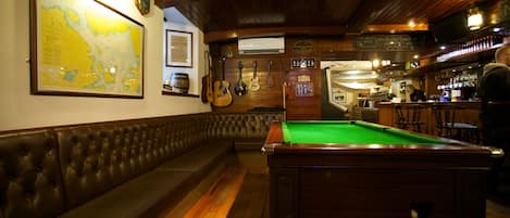 Una mesa de billar en un bar con suelo de madera, un sofá de cuero y un mapa en la pared.
