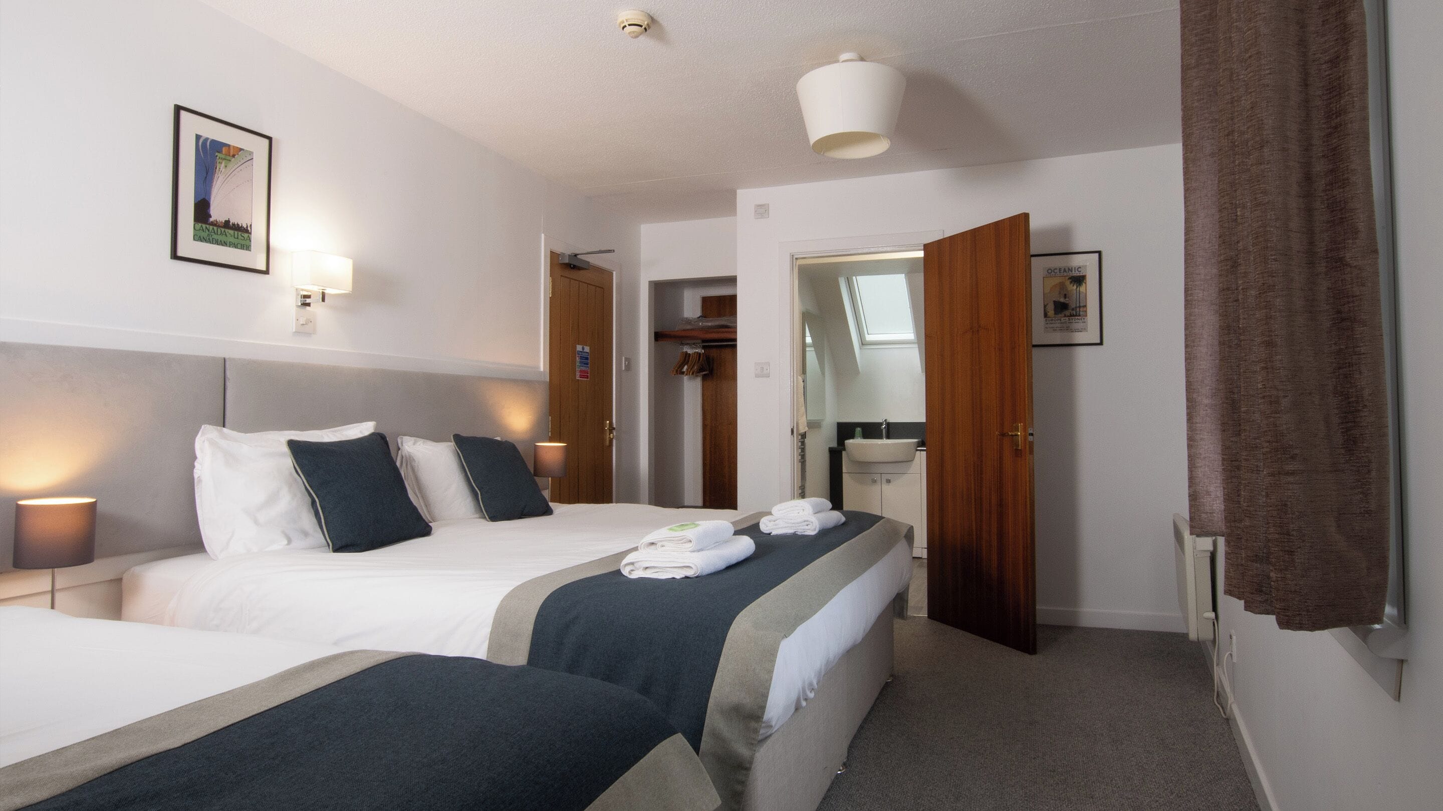 A hotel room with a bed, bedside lamps, a bathroom visible through an open door, and a framed picture on the wall.
