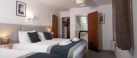 A hotel room with a bed, bedside lamps, a bathroom visible through an open door, and a framed picture on the wall.