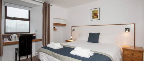 Habitación de hotel con cama, mesitas de noche, escritorio con silla, ventana con cortinas e imagen en la pared.