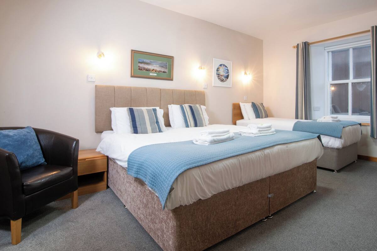 Habitación de hotel con una cama grande, una silla, una mesita de noche y una ventana con cortinas.