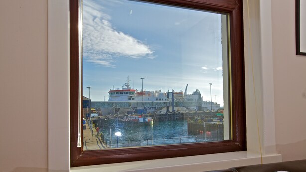 A room with a large window overlooking a harbor, featuring a ship docked at a pier. - Ferry Inn Stromness (Stromness)