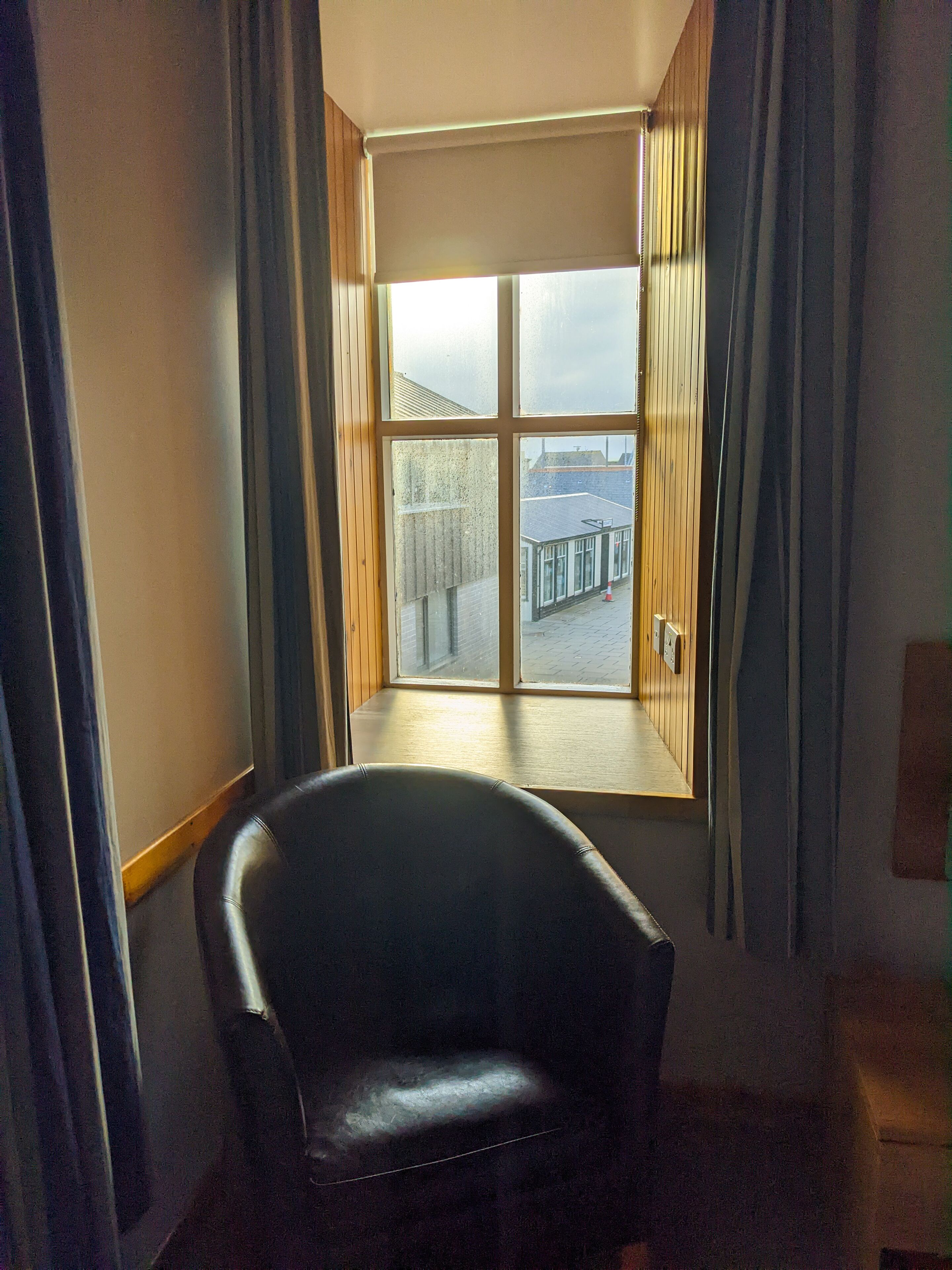 Habitación de esquina con un ventanal grande, una silla y suelo de madera.