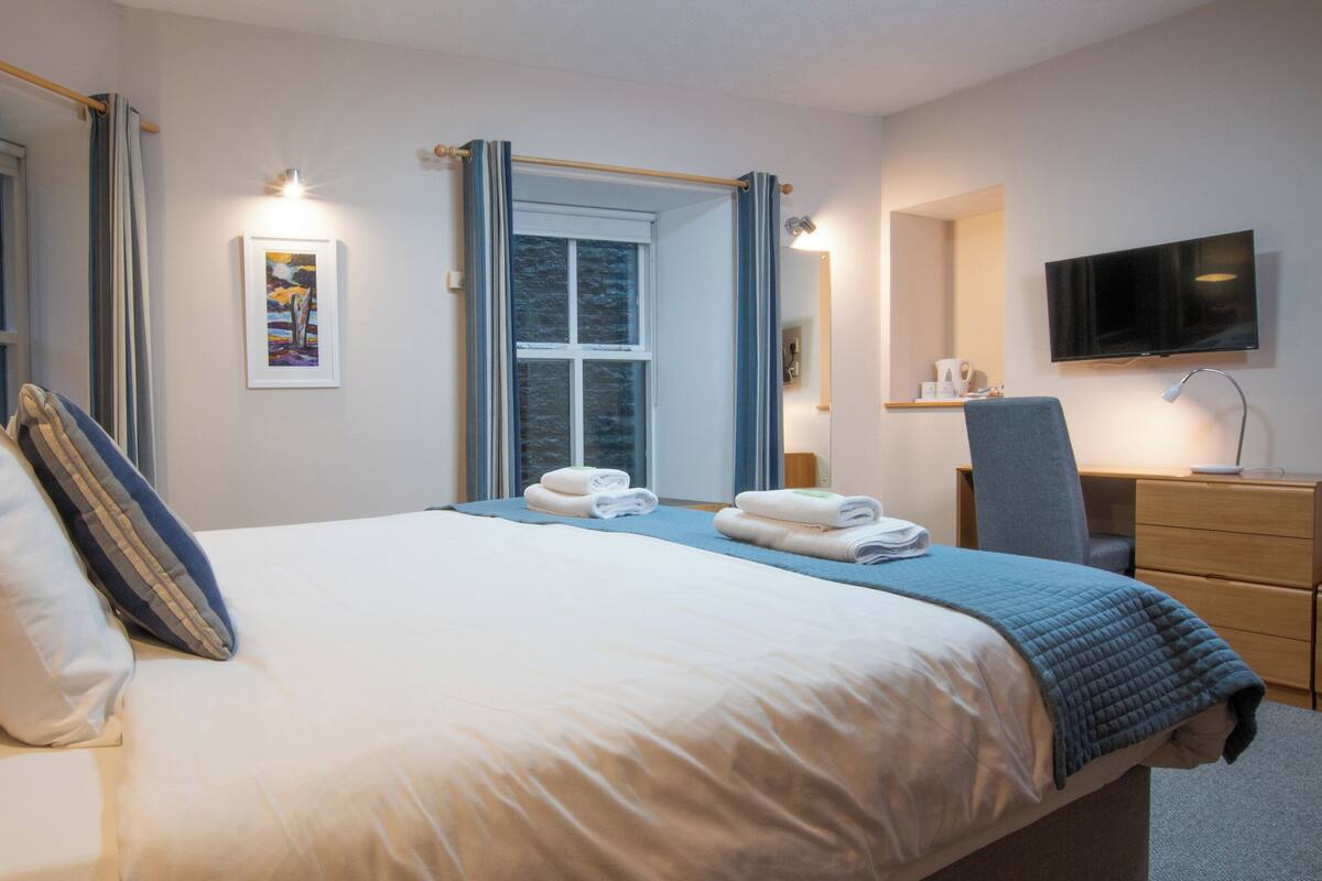 Una habitación de hotel con una cama grande, un escritorio, una silla, un televisor y una ventana con cortinas.