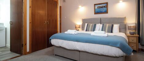 Un dormitorio con una cama grande, un armario de madera, un cuadro en la pared y una mesita de noche con una lámpara.