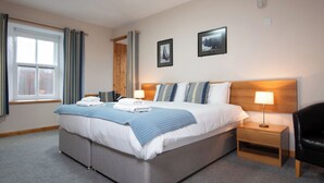 A hotel room with a large bed, two bedside tables, a chair, a window with curtains, and two framed pictures on the wall. - Ferry Inn Stromness (Stromness)