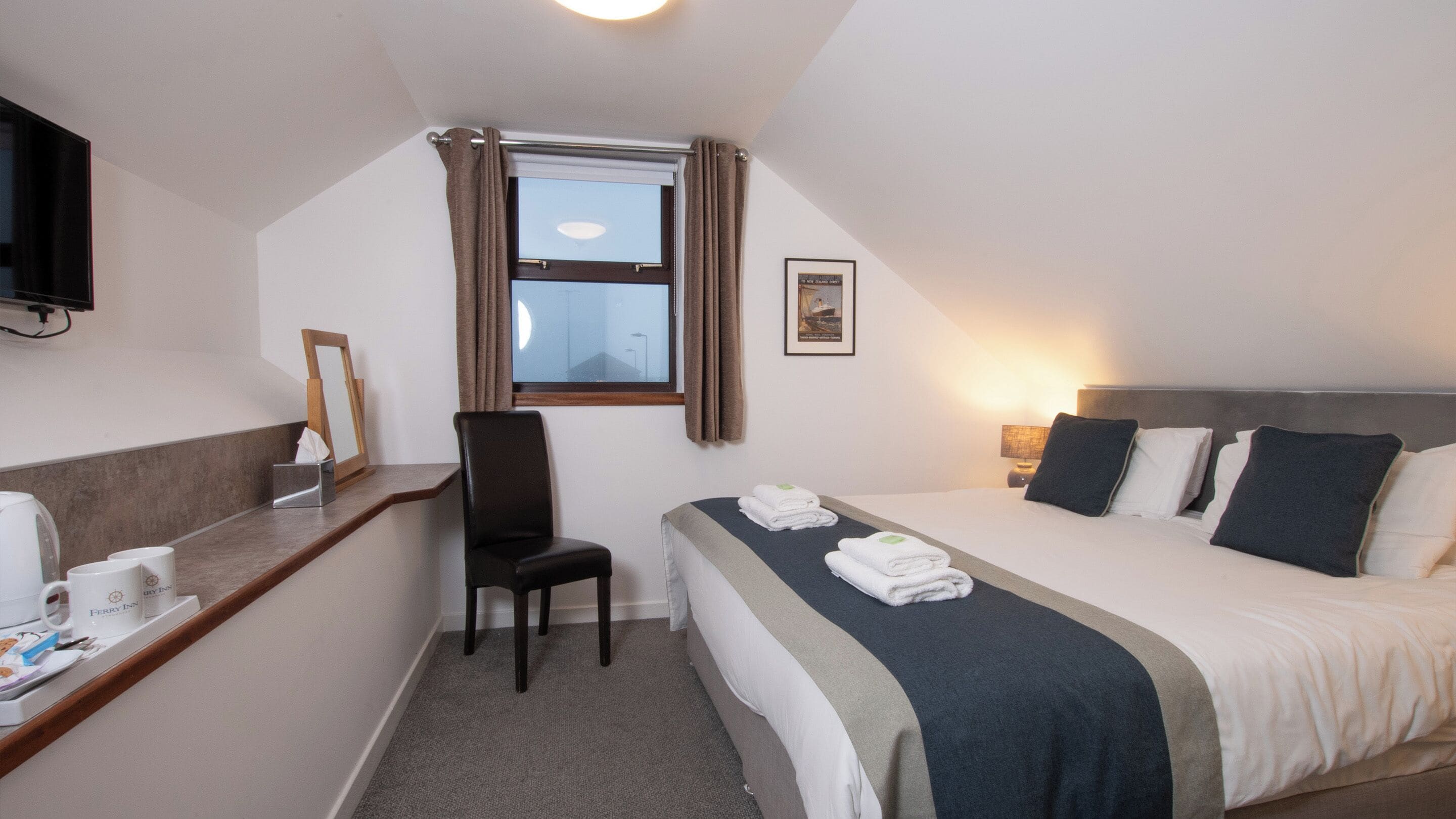 A hotel room with a bed, a desk with a chair, a television, and a window with curtains.