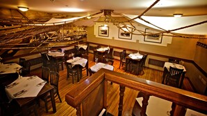 A restaurant with wooden floors, tables set with white tablecloths, and a high ceiling with exposed beams and a hanging light fixture. - Ferry Inn Stromness (Stromness)