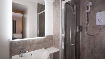 Un baño moderno con un lavabo blanco, cabina de ducha con mampara de vidrio y panel de control en la pared.