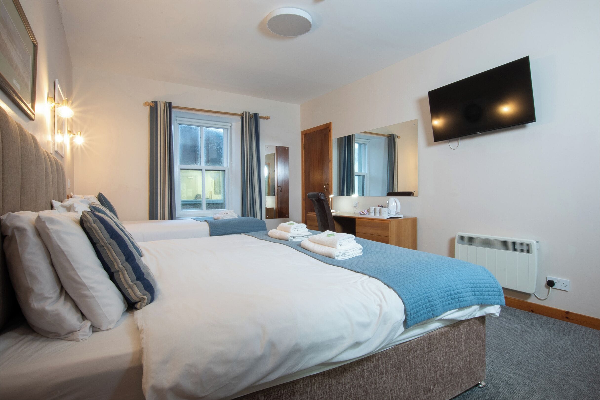 Habitación de hotel con una cama grande, un escritorio, una silla, un televisor de pantalla plana y un ventanal con cortinas.