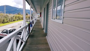 Une terrasse en bois couverte, dotée d’une rambarde, avec un véhicule garé sur la gauche et une vue sur une montagne en arrière-plan.
