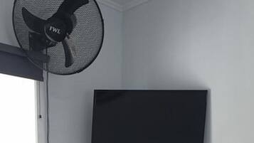 Une chambre avec un lit, un bureau, une chaise, un téléviseur et un ventilateur sur pied.