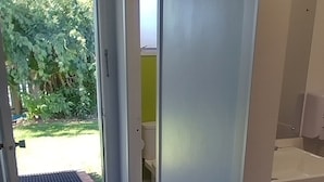 Un couloir au plancher de bois menant à une salle de bain équipée de toilettes et d’un lavabo.