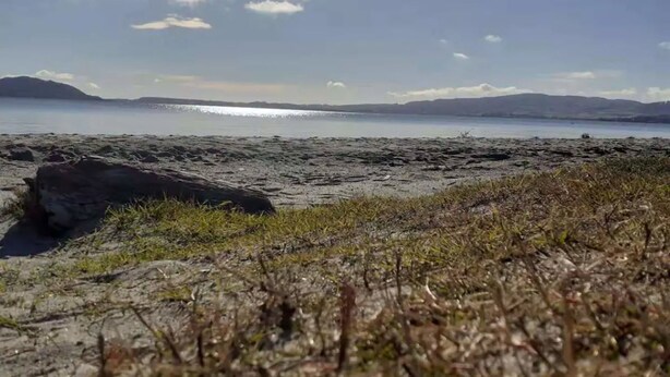 Une plage avec un rivage rocheux au premier plan et une mer calme à l’arrière-plan.