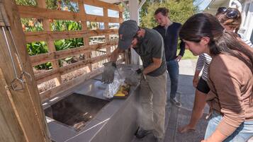 A group of people around a food preparation area with a wooden fence and a tiled floor.
