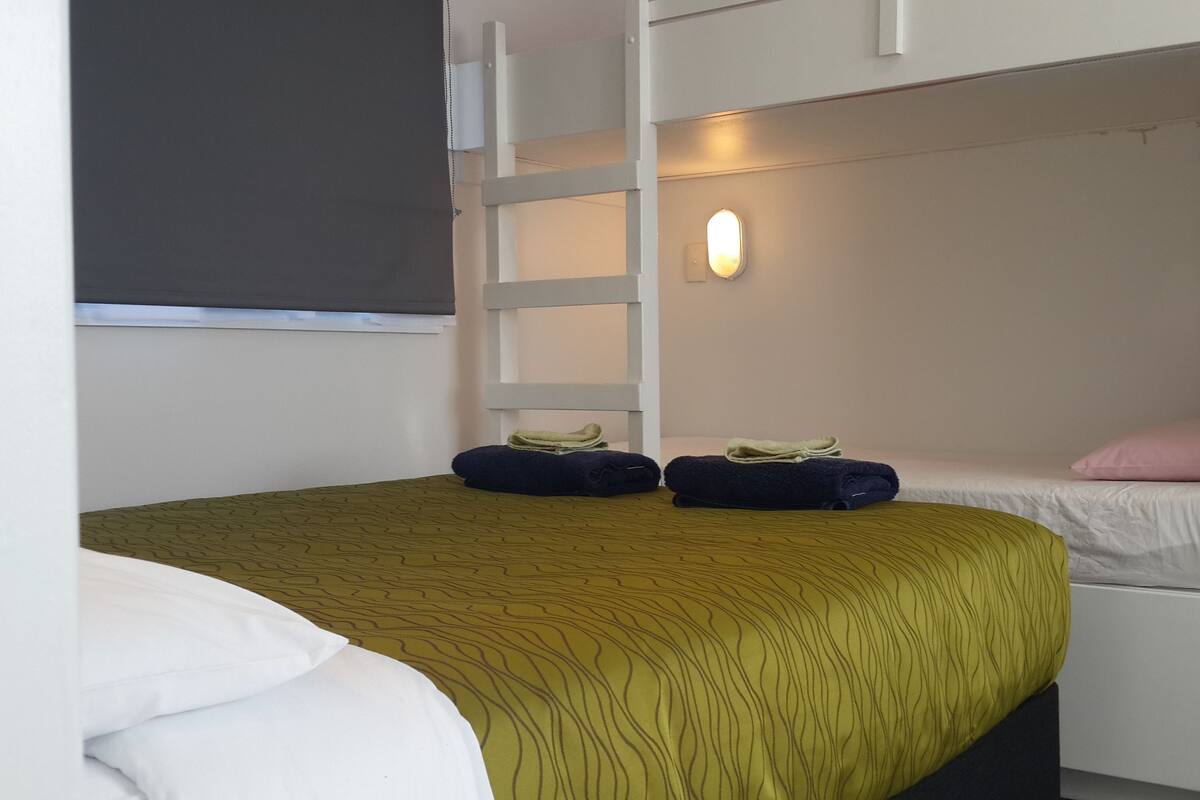 Een slaapkamer met een stapelbed, een bedlampje en twee opgerolde handdoeken op het onderbed.