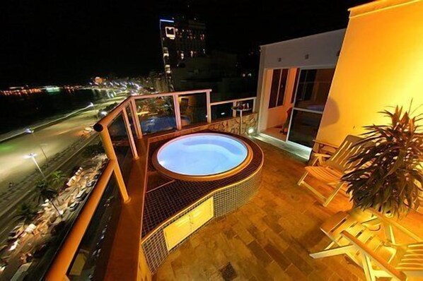 Un jacuzzi sur un balcon avec vue sur la ville, la nuit.