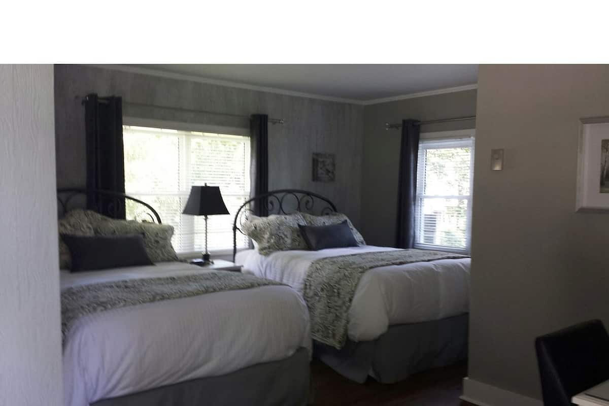 A bedroom with two beds, a nightstand with a lamp, and a window with curtains.