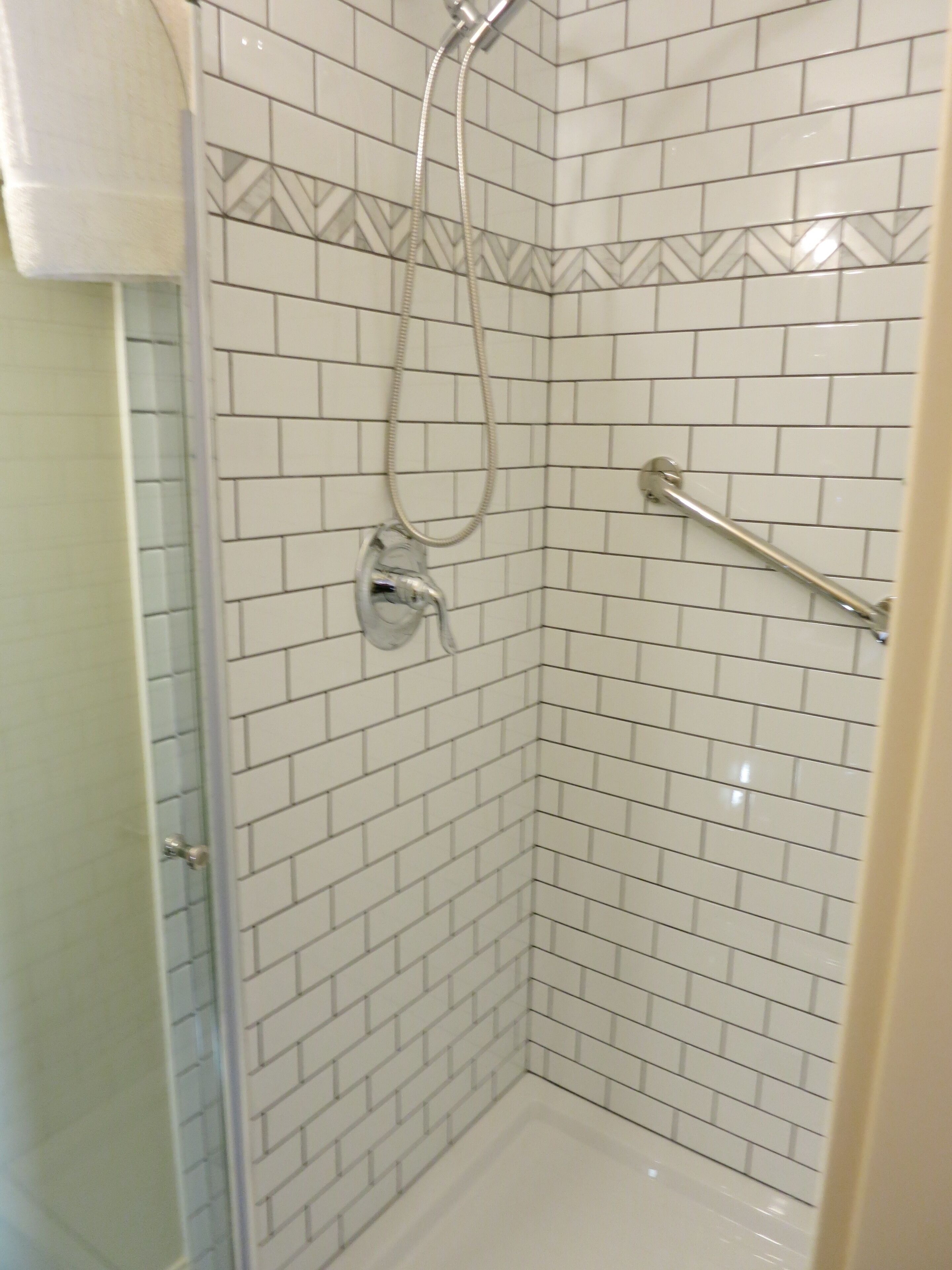 A shower with white tiled walls and a handheld showerhead.