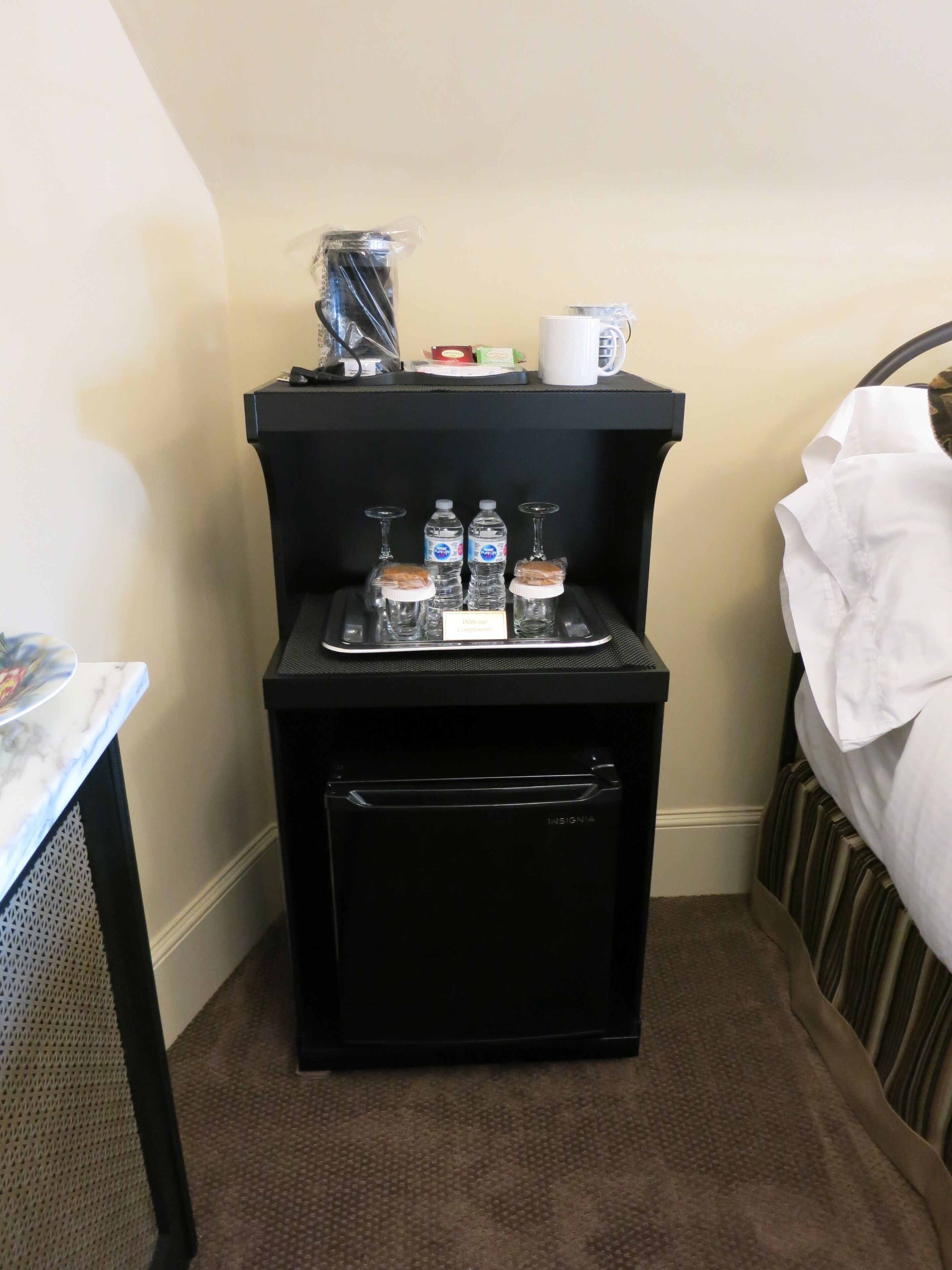 A compact minibar with a selection of bottled water, a wine glass, and a coffee mug.