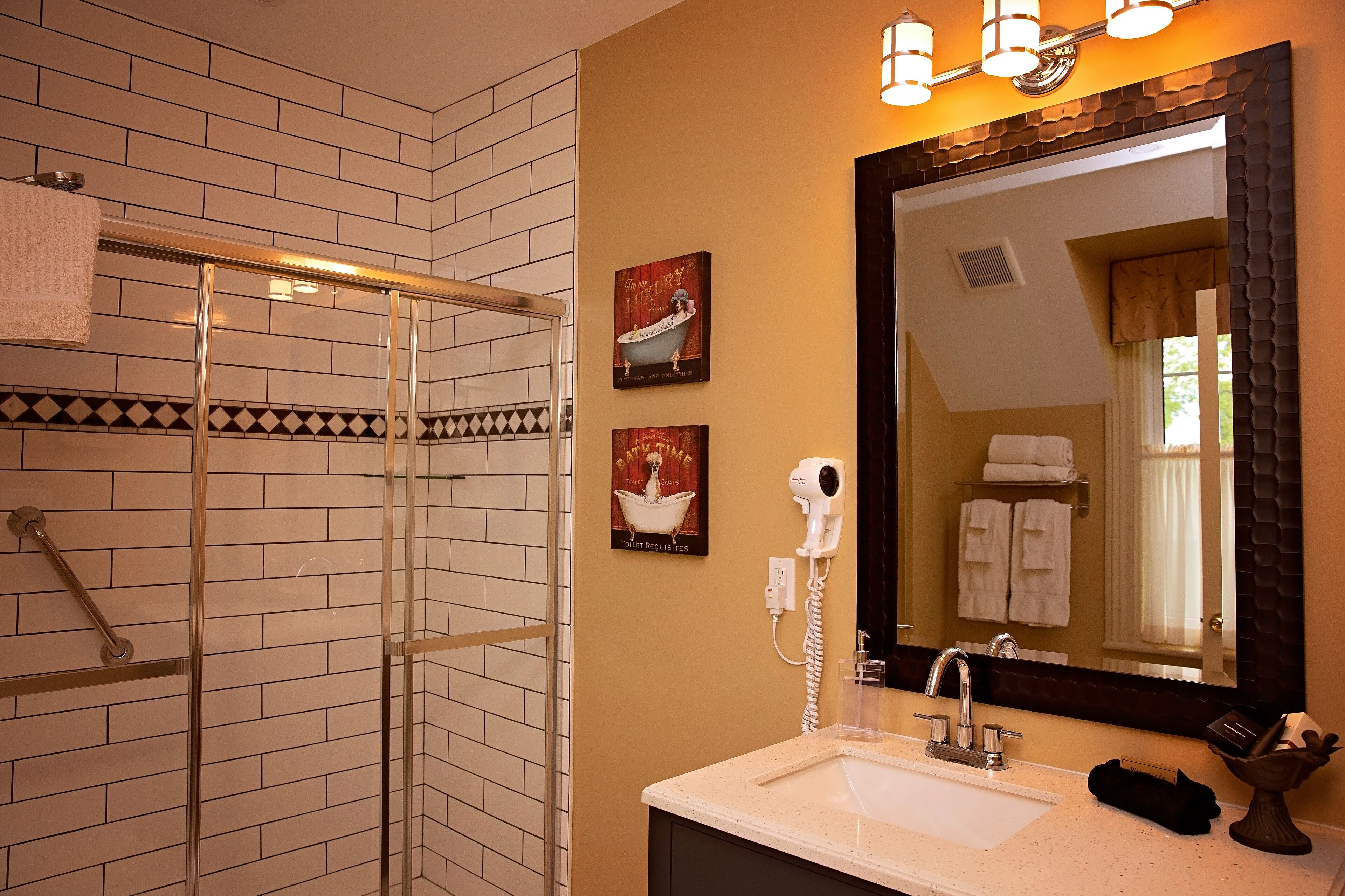 Un baño con cabina de ducha de vidrio, un lavamanos con espejo y dos toalleros de pared.