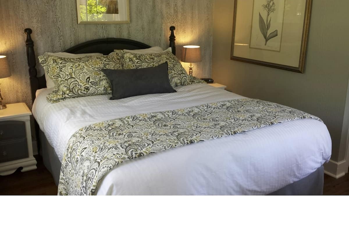 A neatly made bed with patterned bedding, two bedside lamps, a framed botanical print on the wall, and a nightstand with a drawer.