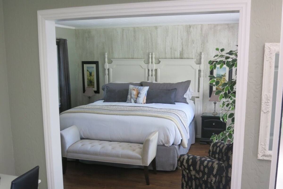 A bedroom with a large bed, a bench, a nightstand, and a chair.