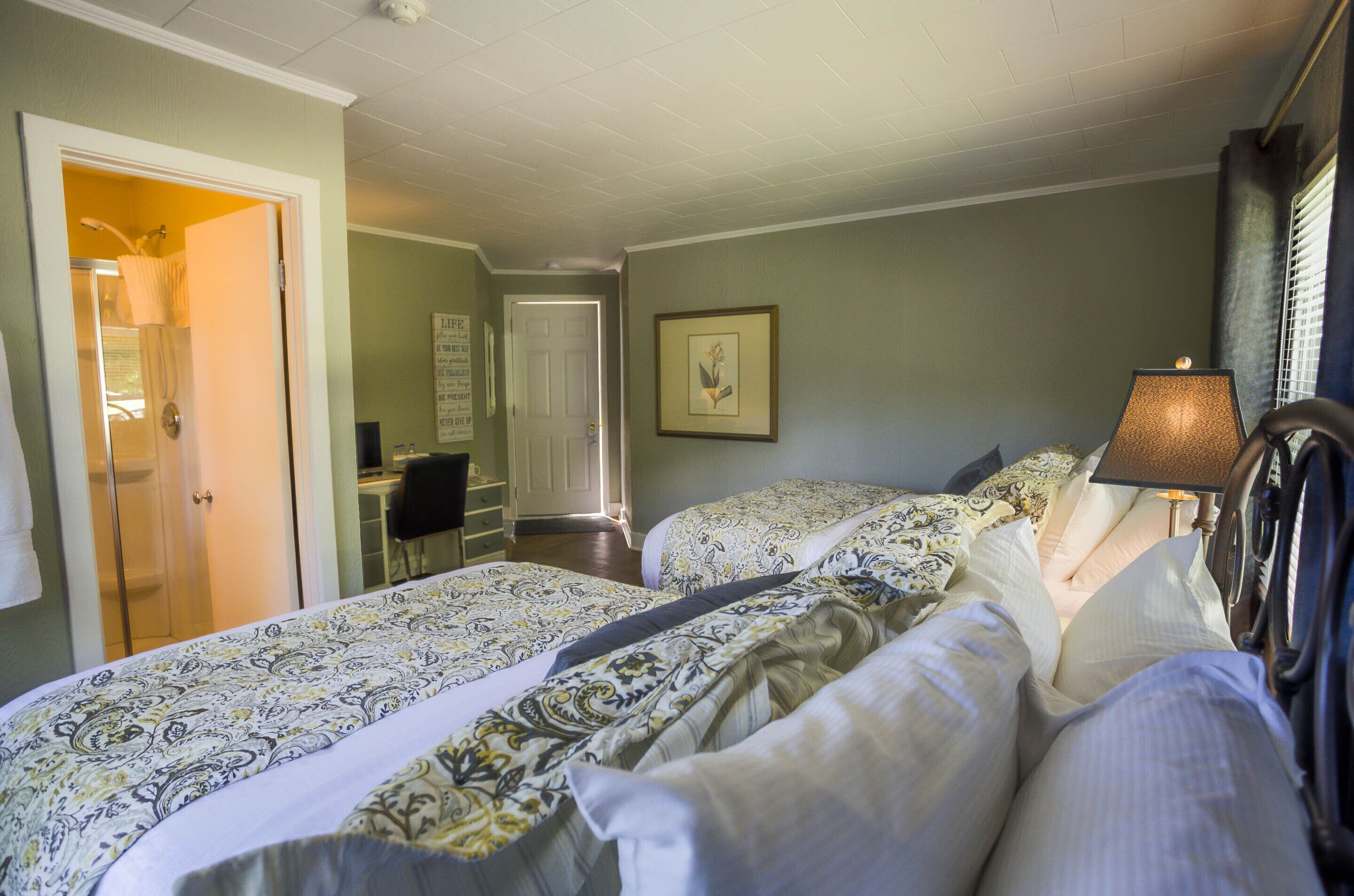 A hotel room with two beds, a desk, and a bathroom.