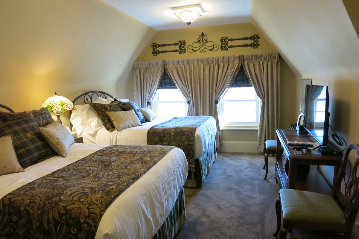A hotel room with two beds, a desk with a chair, a television, and a window with curtains.