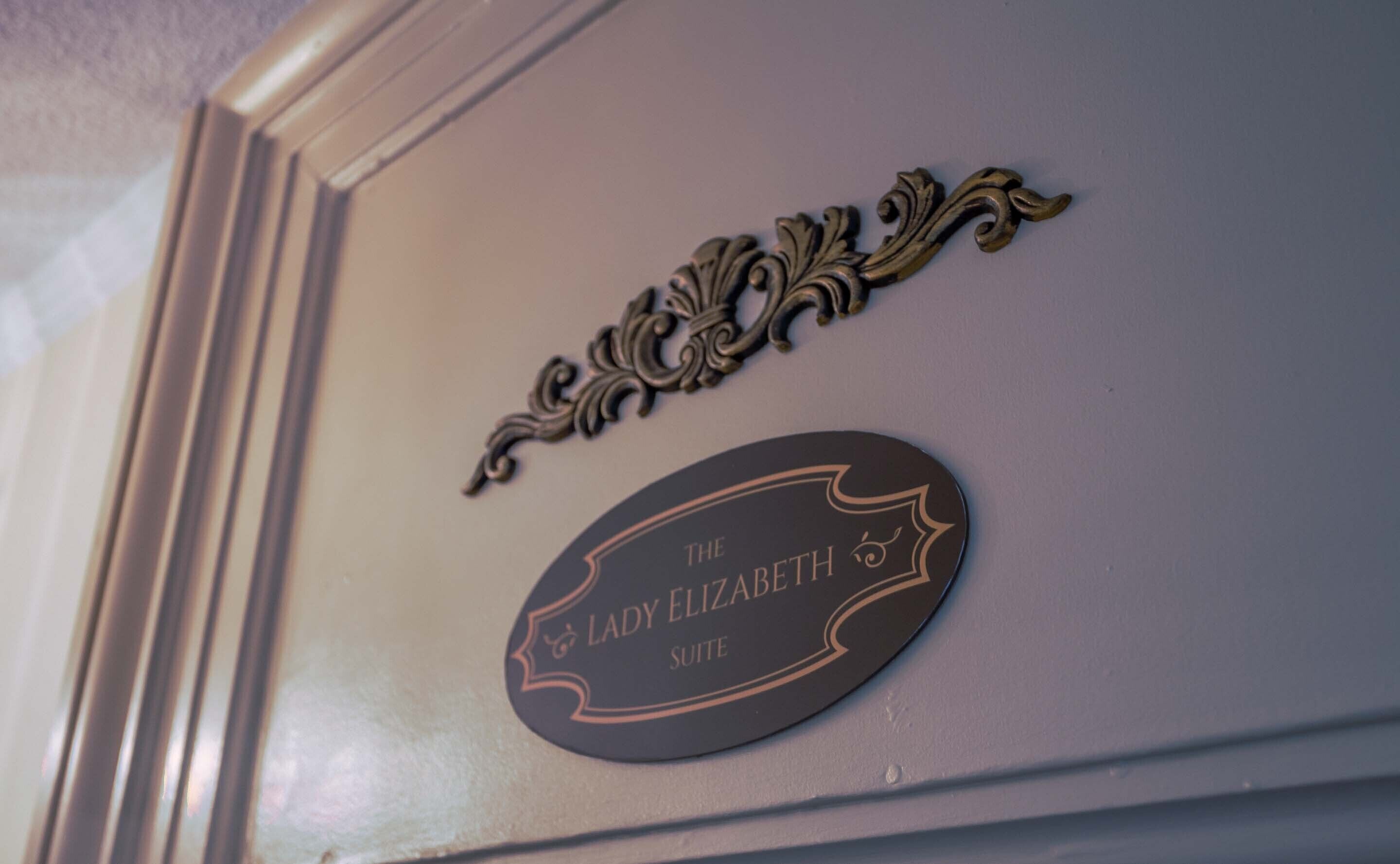 Ein Schild mit der Aufschrift 'The Lady Elizabeth Suite', verziert mit aufwendiger Metallornamentik.