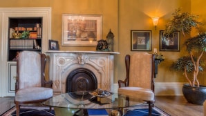 Una habitación tradicional con chimenea, dos sillones, una mesa de centro de vidrio y una estantería.