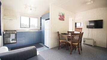 A compact kitchen with a stove, oven, and refrigerator, a dining table with chairs, a sofa, and a TV mounted on the wall.