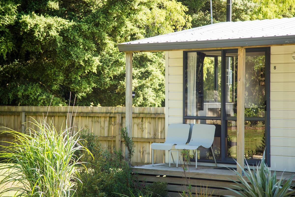 Un espacio de estar techado al aire libre con un banco y un vidrio que da a una casa.