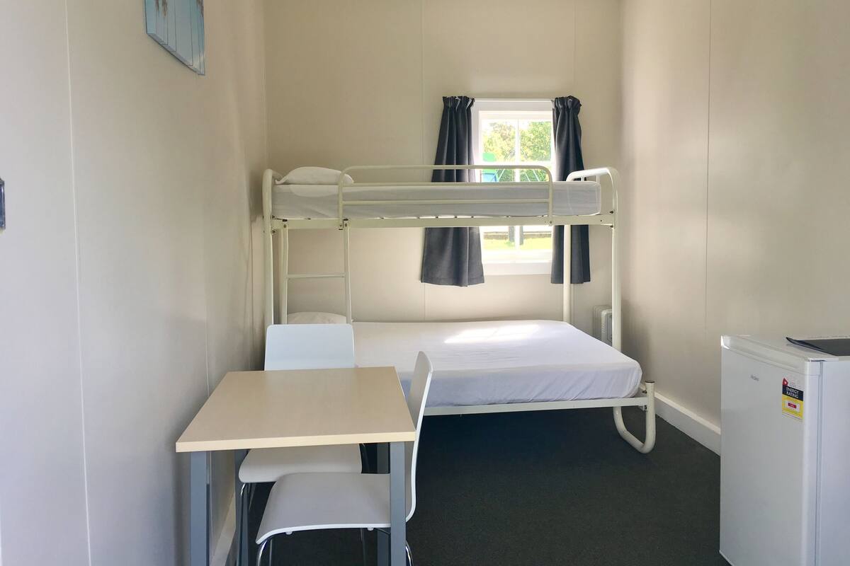 Un dormitorio con literas, un escritorio, una silla y un refrigerador.