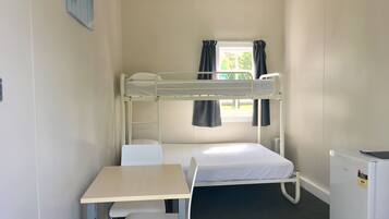 A bunk room with a bunk bed, a desk, a chair, and a refrigerator.