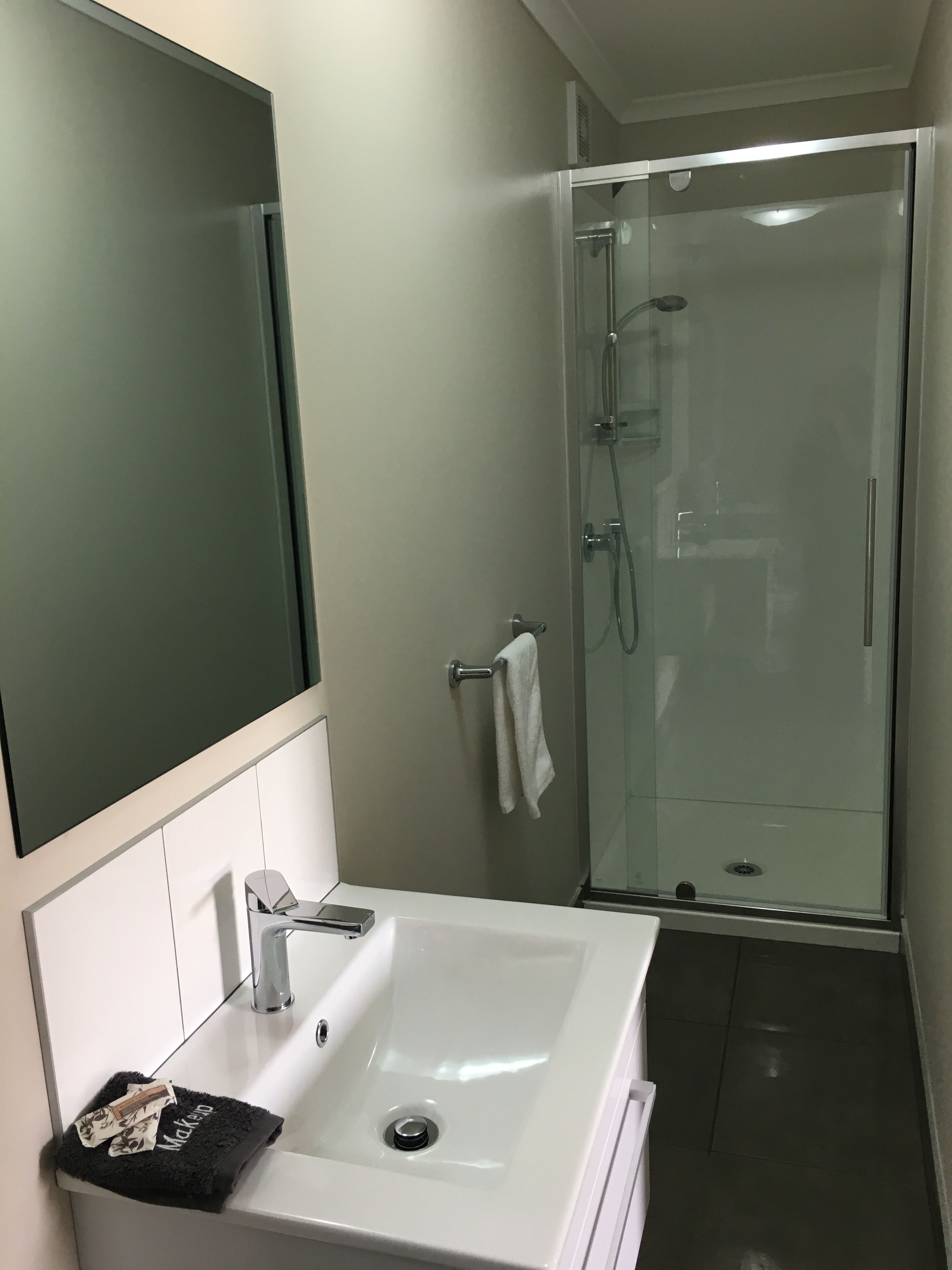 Un baño moderno con un lavamanos blanco, un espejo grande y una ducha con cerramiento de vidrio.