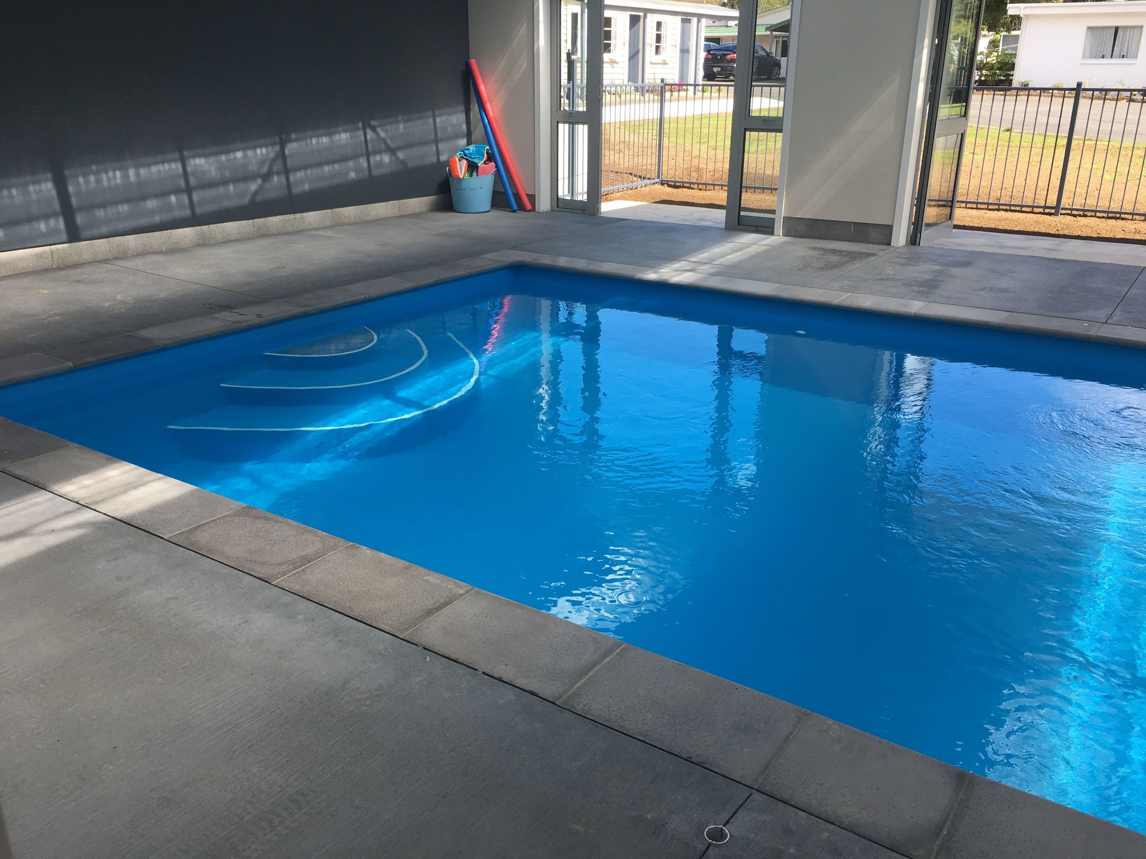 A rectangular swimming pool with clear blue water, surrounded by a concrete deck.
