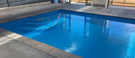 A rectangular swimming pool with clear blue water, surrounded by a concrete deck.