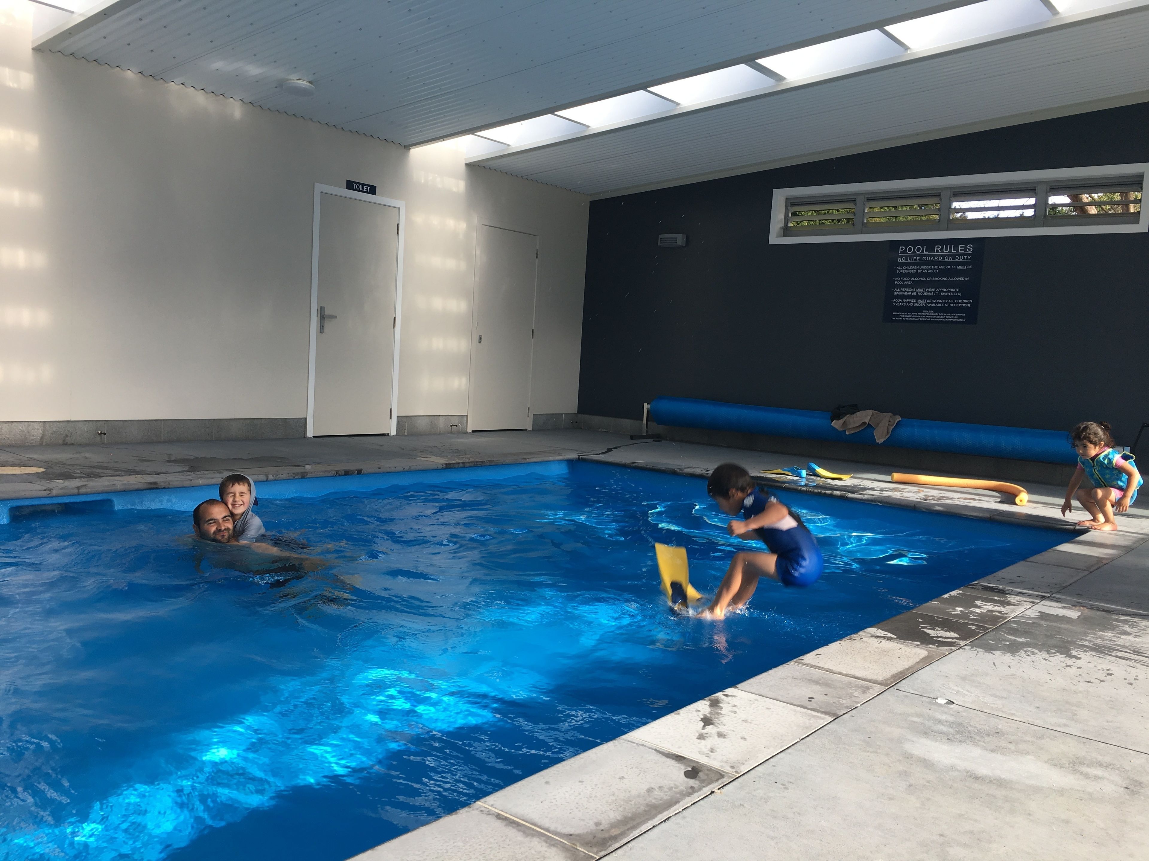 Une piscine intérieure à l’eau claire, un plafond doté de lucarnes et un panneau indiquant les règles de la piscine.