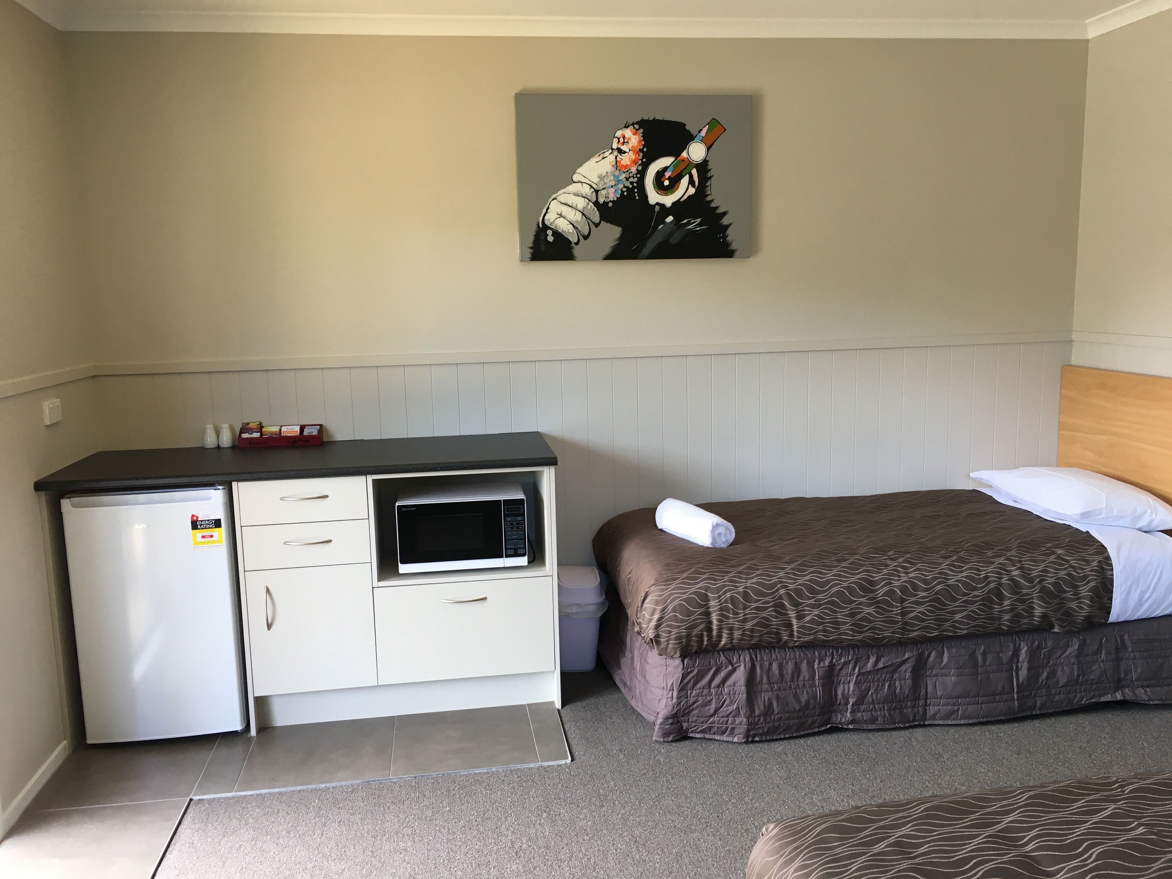 Una habitación compacta con kitchenette, una cama con colcha marrón estampada y un cuadro en la pared.